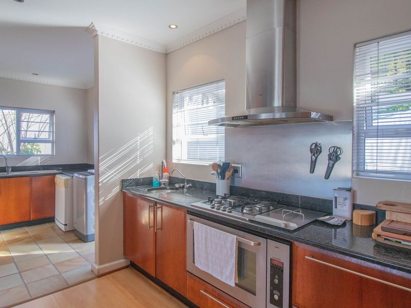 A well-maintained kitchen featuring granite countertops, wooden cabinetry, built-in oven, gas hob, and a separate scullery area with additional sink and storage.