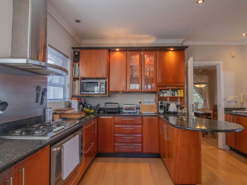 A well-appointed kitchen featuring warm-toned wooden cabinetry, granite countertops, a gas hob, and integrated appliances, offering a functional and classic cooking space.