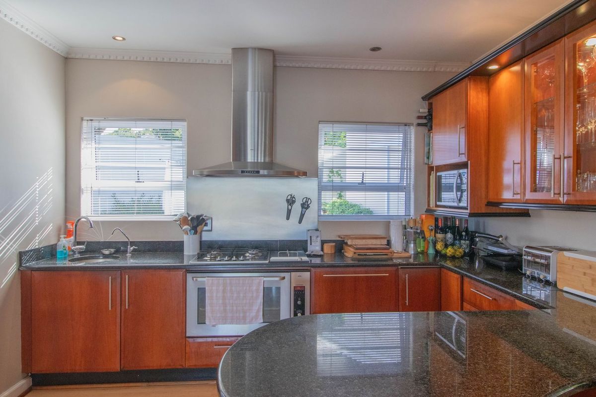 A well-appointed kitchen featuring granite countertops, wooden cabinetry, a stainless steel extractor fan, and a built-in oven with a gas hob.