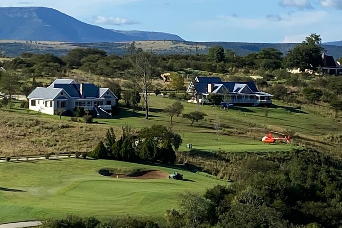 An aerial view of a residential estate featuring golf course fairways, bunkers, and surrounding homes set against a mountainous landscape.