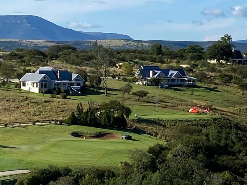 An aerial view of a residential estate featuring golf course fairways, bunkers, and surrounding homes set against a mountainous landscape.