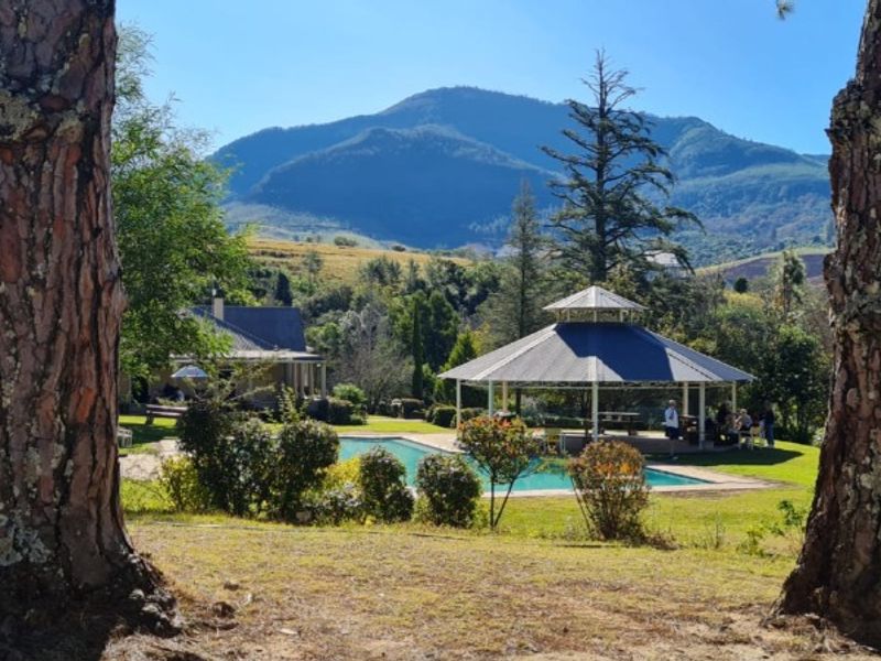 Scenic view of a swimming pool and gazebo set against a backdrop of rolling mountains and lush greenery.
