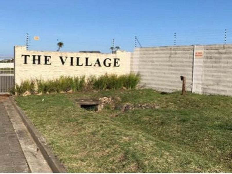 Entrance view of The Village residential estate featuring a perimeter wall, electric fencing, and a secure sliding gate.
