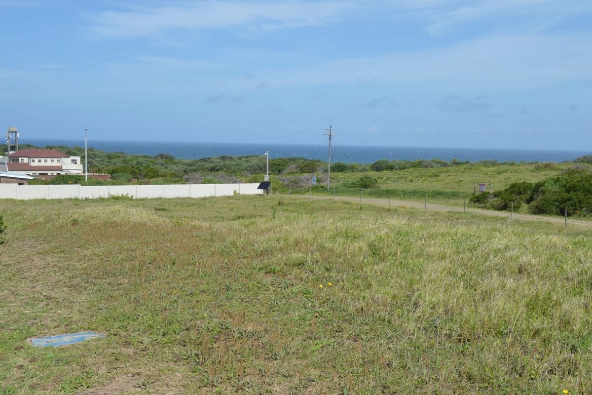 A view of a vacant residential plot featuring natural grass terrain, perimeter fencing, and distant ocean views.