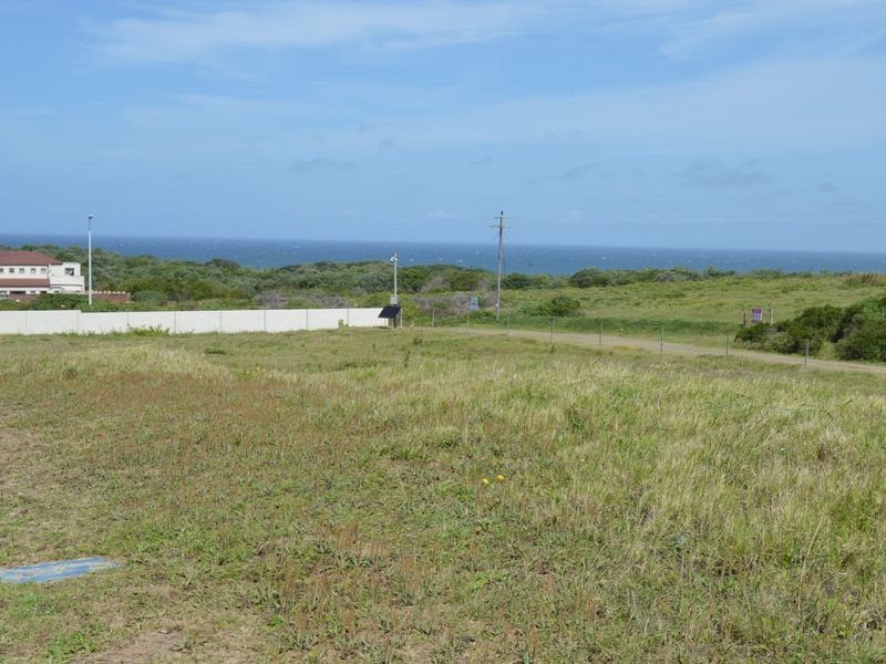 A view of a vacant residential plot featuring natural grass terrain, perimeter fencing, and distant ocean views.