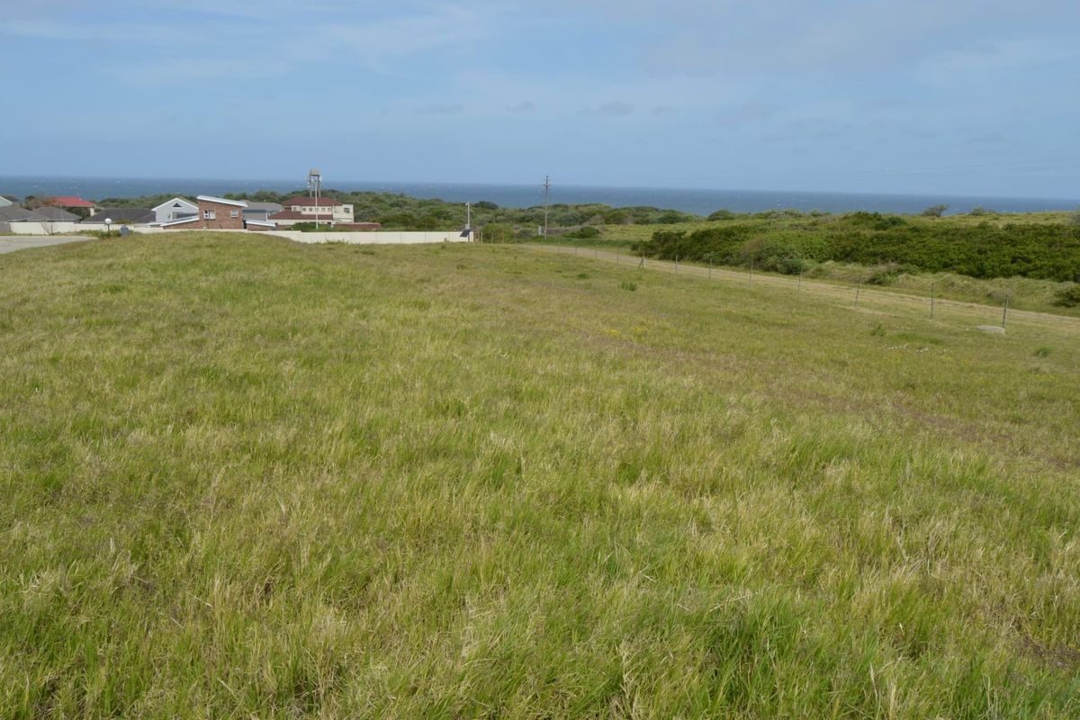 A vacant residential plot featuring expansive grassy terrain with distant ocean views and surrounding coastal landscape.