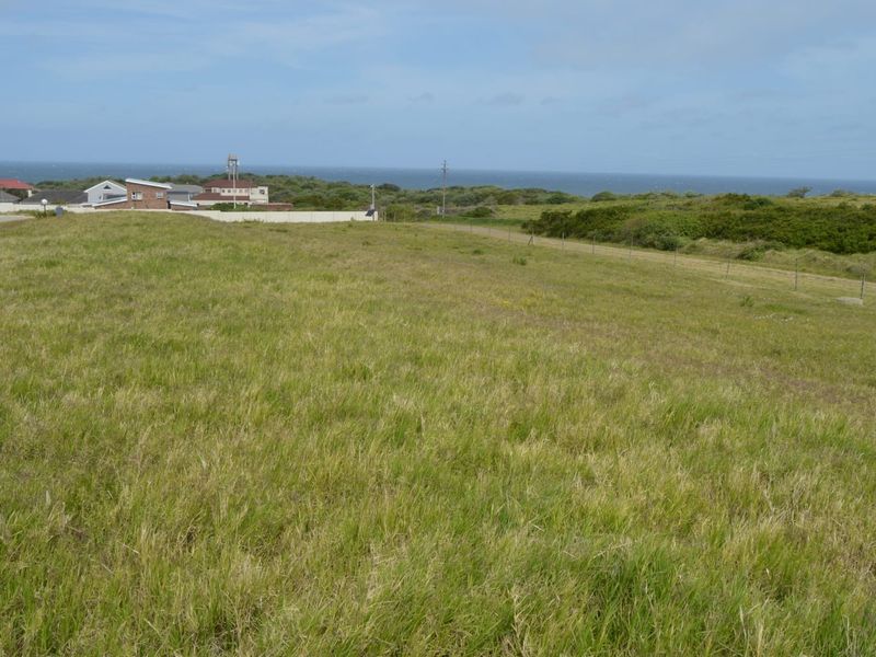 A vacant residential plot featuring expansive grassy terrain with distant ocean views and surrounding coastal landscape.