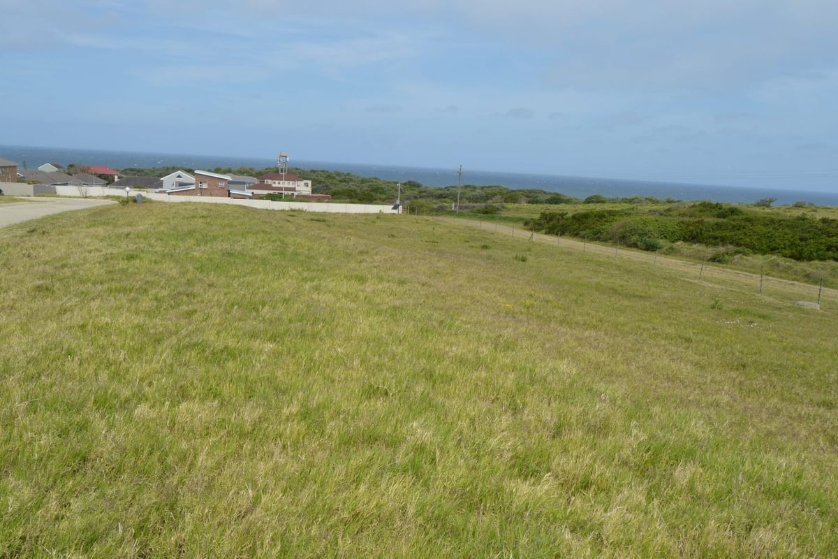 A wide-angle view of a vacant residential plot featuring natural grass cover and distant coastal scenery.