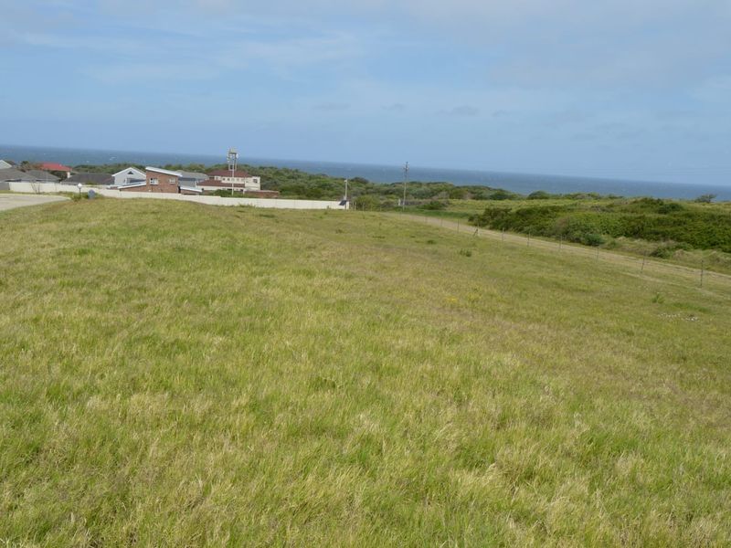 A wide-angle view of a vacant residential plot featuring natural grass cover and distant coastal scenery.