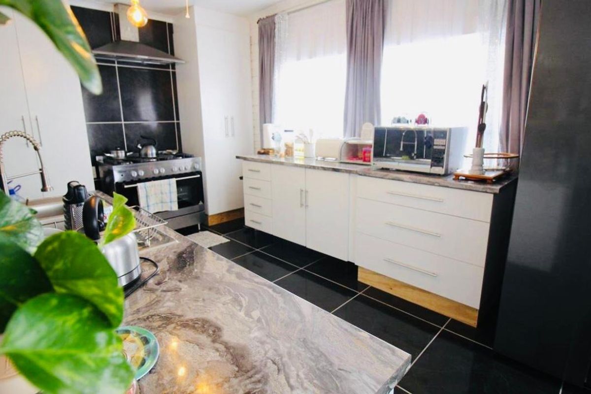 Modern kitchen featuring stone countertops, white cabinetry, gas stove with extractor fan, and dark tiled flooring.