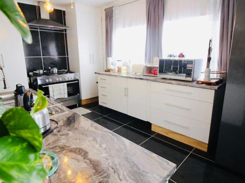 Modern kitchen featuring stone countertops, white cabinetry, gas stove with extractor fan, and dark tiled flooring.