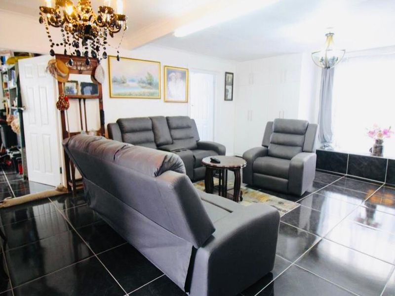 Spacious living room featuring dark polished floor tiles, built-in storage cupboards, and decorative chandelier lighting.