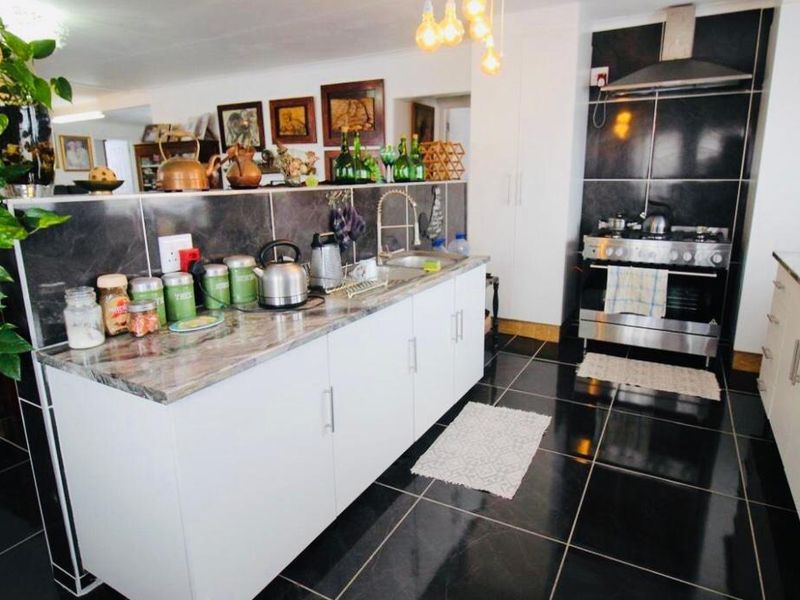 Modern kitchen featuring white cabinetry, stone countertops, a gas stove with extractor fan, and dark tiled flooring in an open-plan layout.