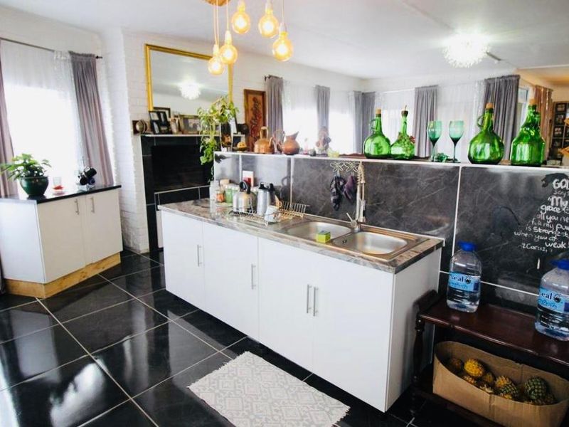 A functional kitchen area featuring white cabinetry, a double sink, stone-look countertops, and dark tiled flooring, illuminated by modern pendant lighting.
