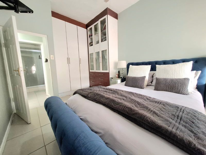 A well-maintained bedroom featuring built-in cupboards, tiled flooring, and direct access to an en-suite bathroom.