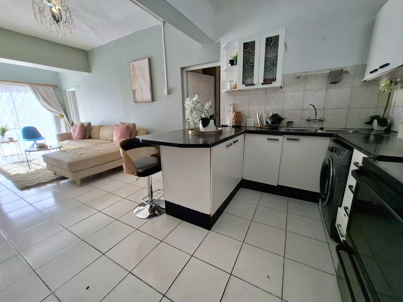 Open-plan living area featuring a functional kitchen with built-in cabinetry, tiled flooring, and a breakfast nook island, seamlessly connecting to the lounge space.