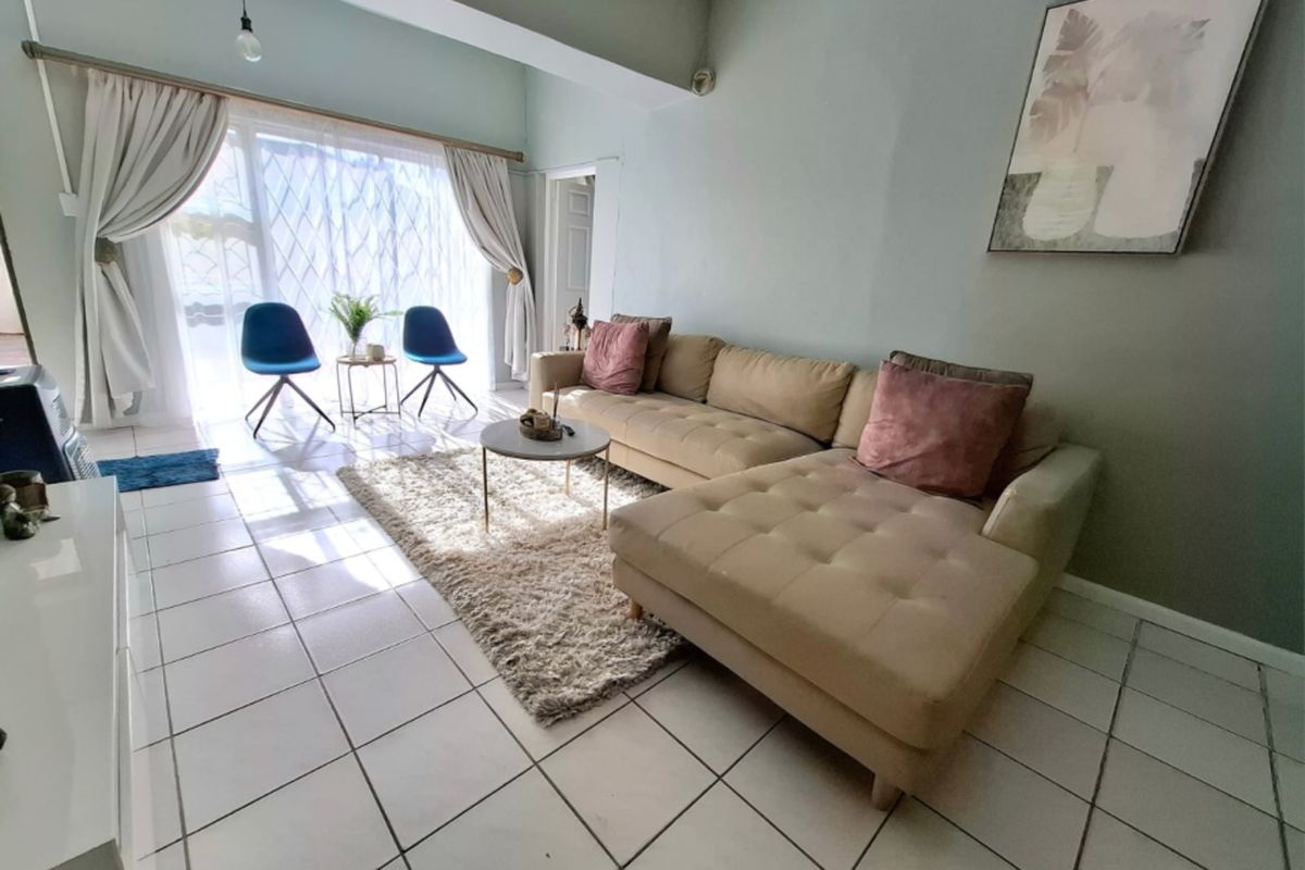 A bright living room featuring tiled flooring, an exposed ceiling beam, and a large sliding glass door providing natural light.