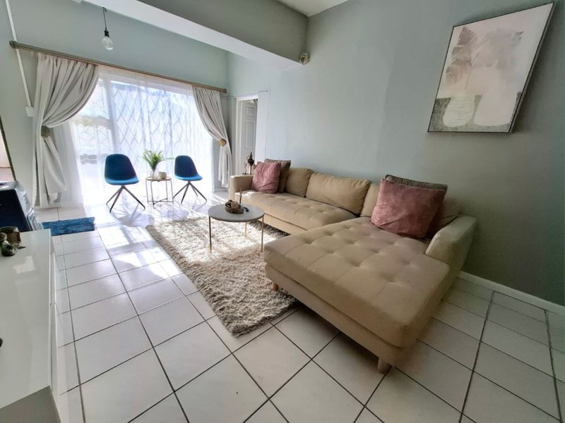 A bright living room featuring tiled flooring, an exposed ceiling beam, and a large sliding glass door providing natural light.