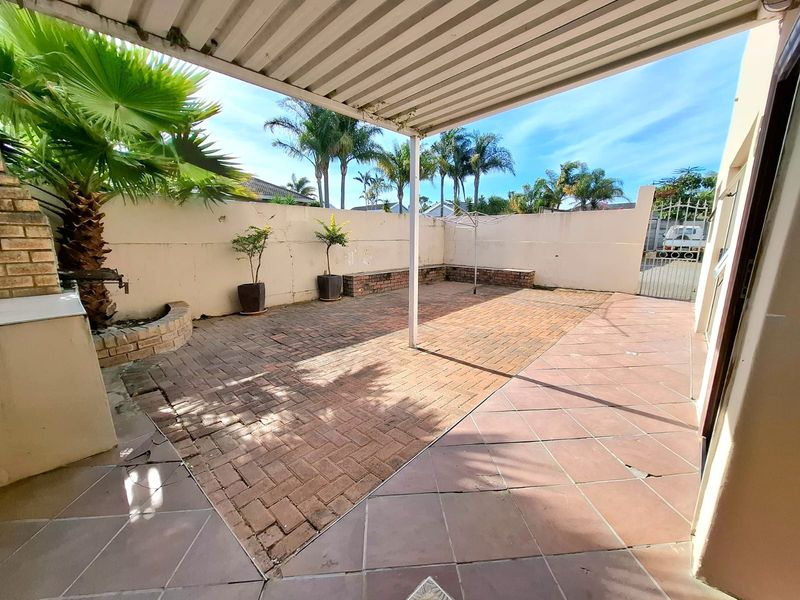 A paved and tiled outdoor patio area featuring a built-in braai, covered roof structure, and enclosed perimeter walling.