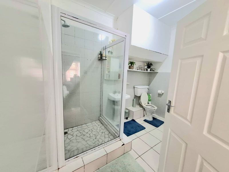 A functional bathroom featuring a glass-enclosed shower, pedestal basin, and toilet with tiled finishes and built-in shelving.