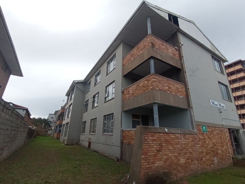 Exterior view of the apartment building showing brick and rendered facade, multiple balconies, and surrounding grounds.