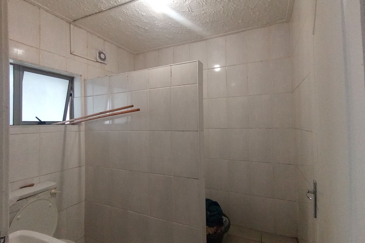 A functional bathroom featuring tiled walls and flooring, a privacy partition, and a top-hung window, currently in need of cosmetic updates.