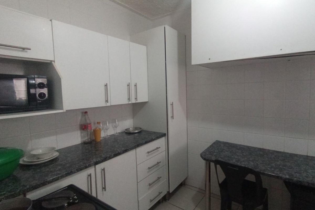 A functional kitchen featuring white cabinetry, dark laminate countertops, tiled backsplash, and tiled flooring with a small integrated breakfast nook area.