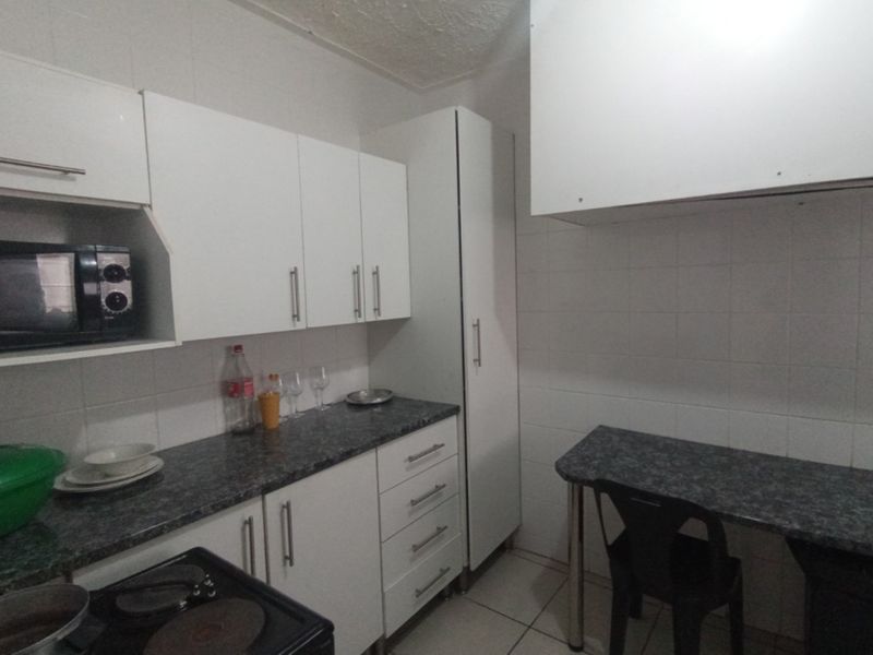 A functional kitchen featuring white cabinetry, dark laminate countertops, tiled backsplash, and tiled flooring with a small integrated breakfast nook area.