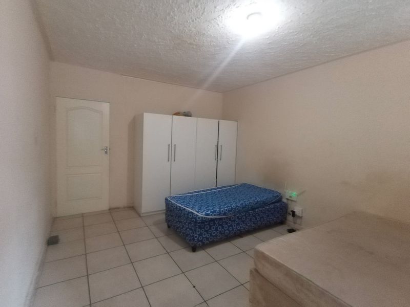 A simple bedroom featuring tiled flooring, a built-in wardrobe, and a textured ceiling, offering a functional space ready for updates.