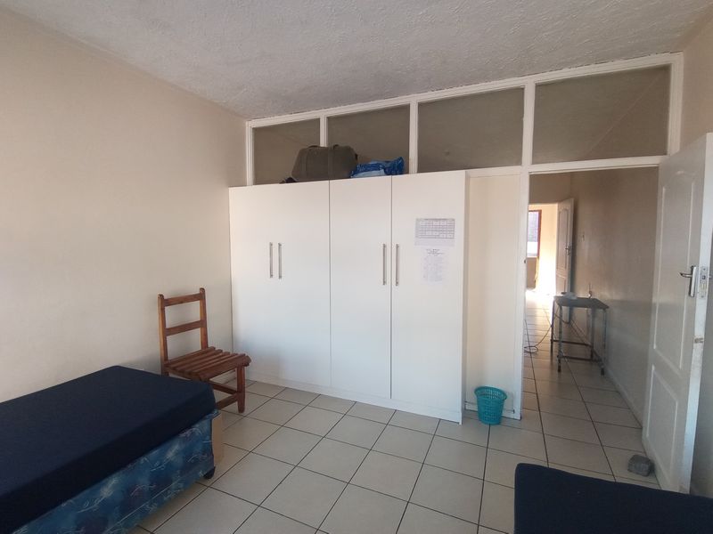A bedroom featuring built-in cupboards with overhead storage and tiled flooring, leading into an adjacent hallway area.
