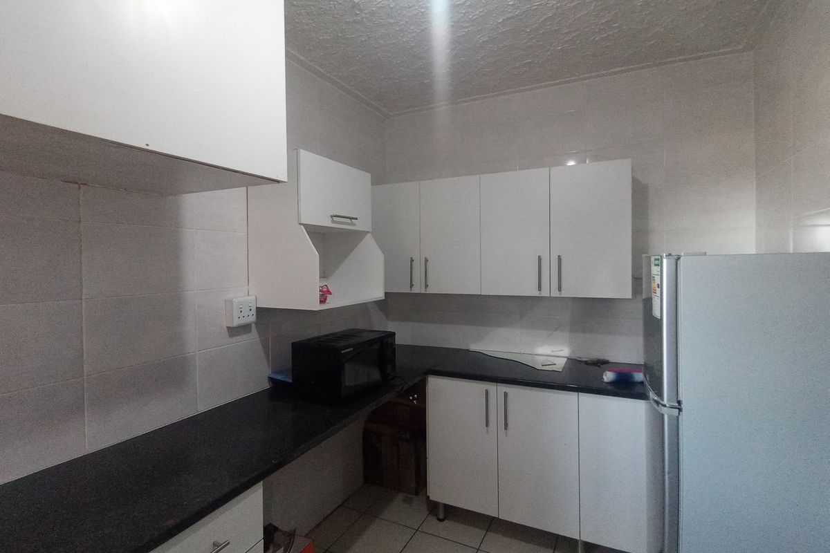 A functional kitchen featuring white cabinetry, black countertops, tiled backsplash, and tiled flooring, providing a clean and practical workspace.