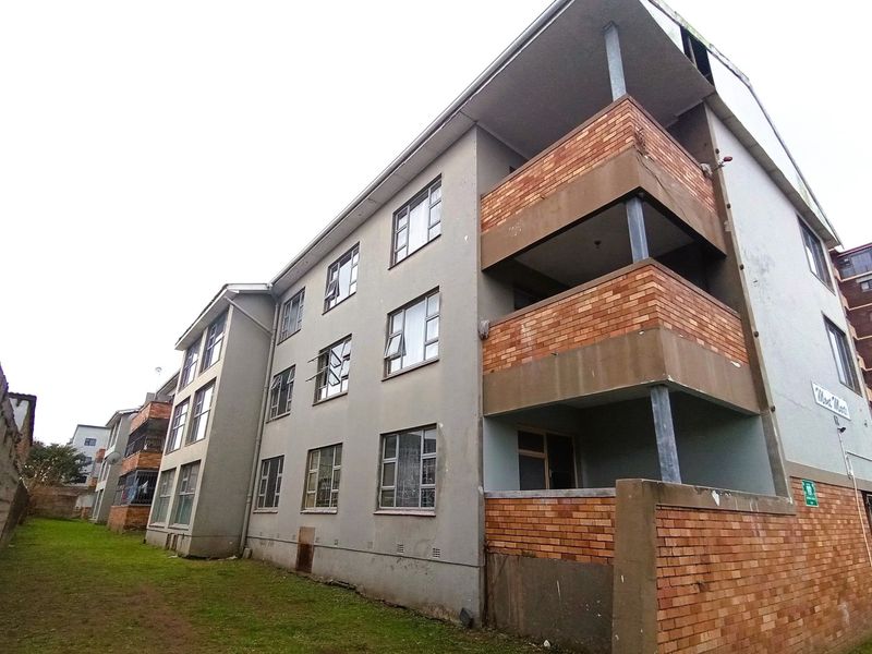 Rear view of a multi-story apartment building featuring brick balconies, metal-framed windows, and a shared grass area.