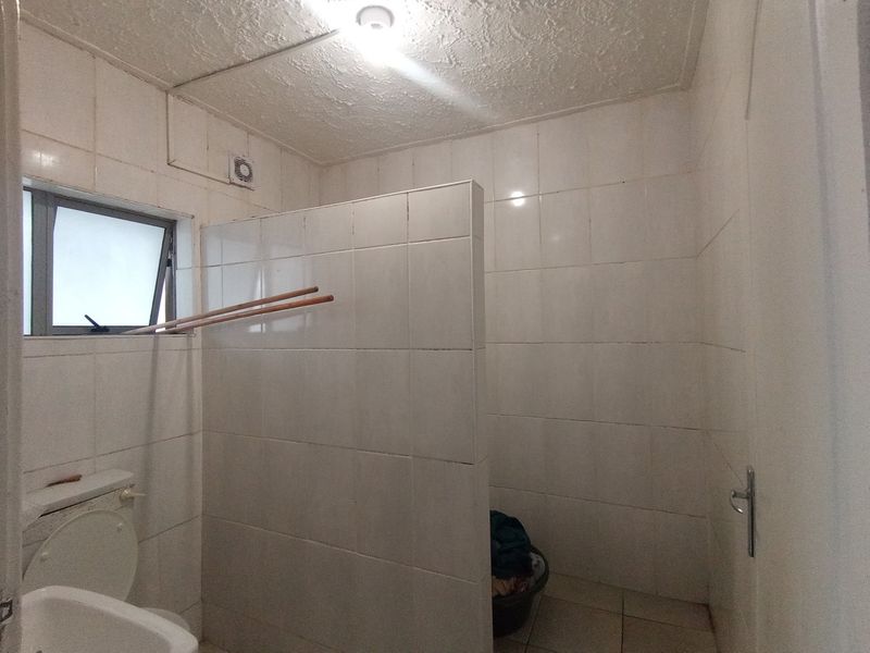 A functional bathroom featuring tiled walls and flooring, a privacy partition, and a top-hung window, currently in need of cosmetic updates.
