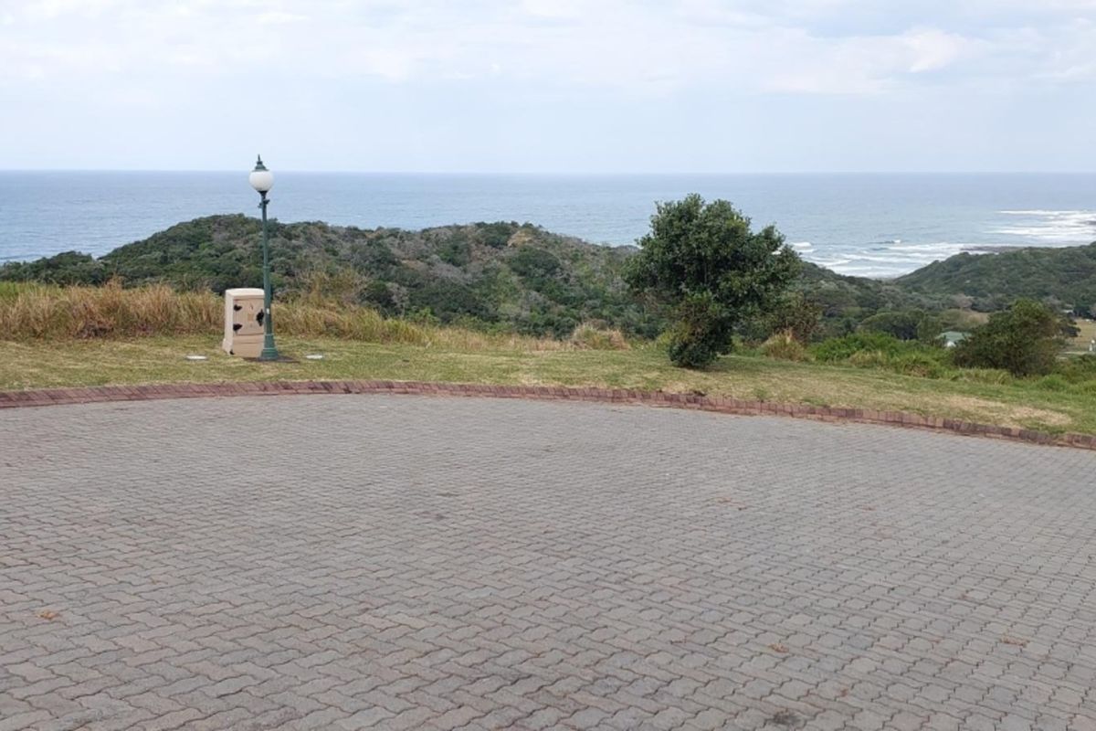 A scenic view of the coastline and rolling hills from a paved residential plot, featuring established street lighting and open landscape.