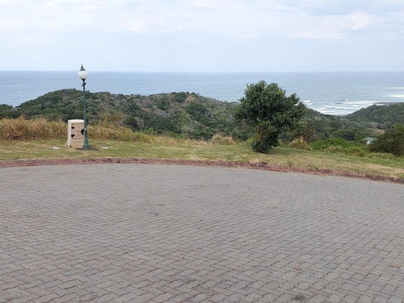 A scenic view of the coastline and rolling hills from a paved residential plot, featuring established street lighting and open landscape.