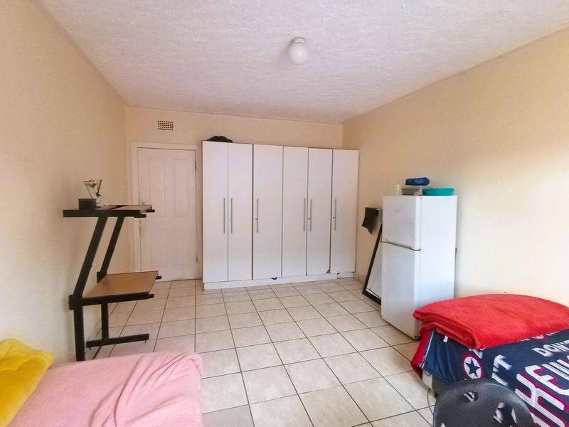 A bedroom featuring tiled flooring and a large built-in wardrobe with some visible wear to the base.