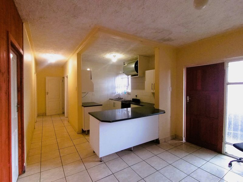 Open-plan kitchen and living area featuring tiled flooring, built-in cabinetry, and a breakfast island, requiring cosmetic updates to the ceiling and walls.