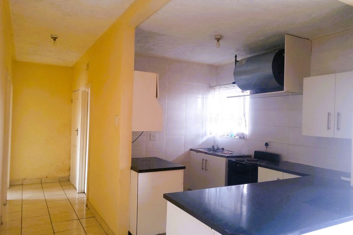 A functional kitchen featuring built-in cabinetry, laminate countertops, and a tiled backsplash, currently vacant and ready for cosmetic updates.
