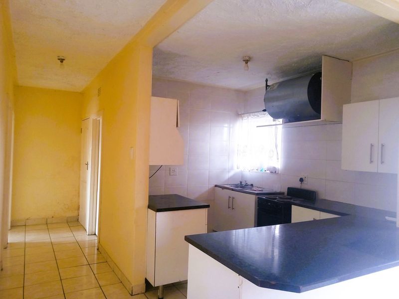 A functional kitchen featuring built-in cabinetry, laminate countertops, and a tiled backsplash, currently vacant and ready for cosmetic updates.
