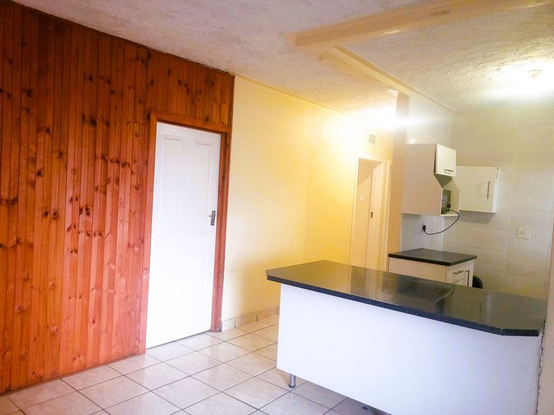 Open plan living and kitchen area featuring tiled flooring, granite countertops, and timber wall paneling, offering a functional space ready for modernization.