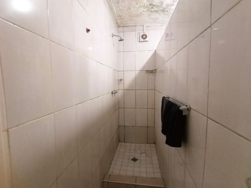 A compact shower stall featuring white wall tiles and a tiled floor, currently showing signs of ceiling water damage and wear.