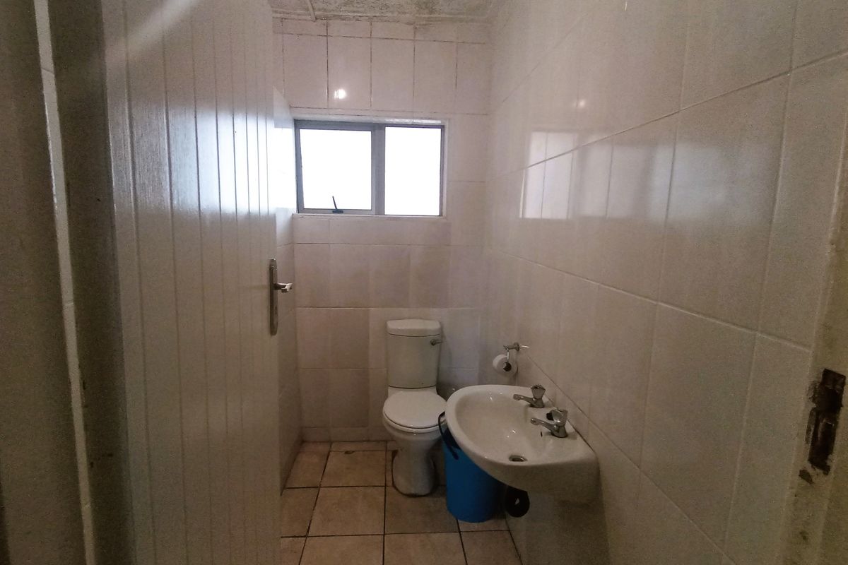 A compact bathroom featuring tiled walls and flooring, a pedestal basin, and a standard toilet, requiring cosmetic updates and maintenance.