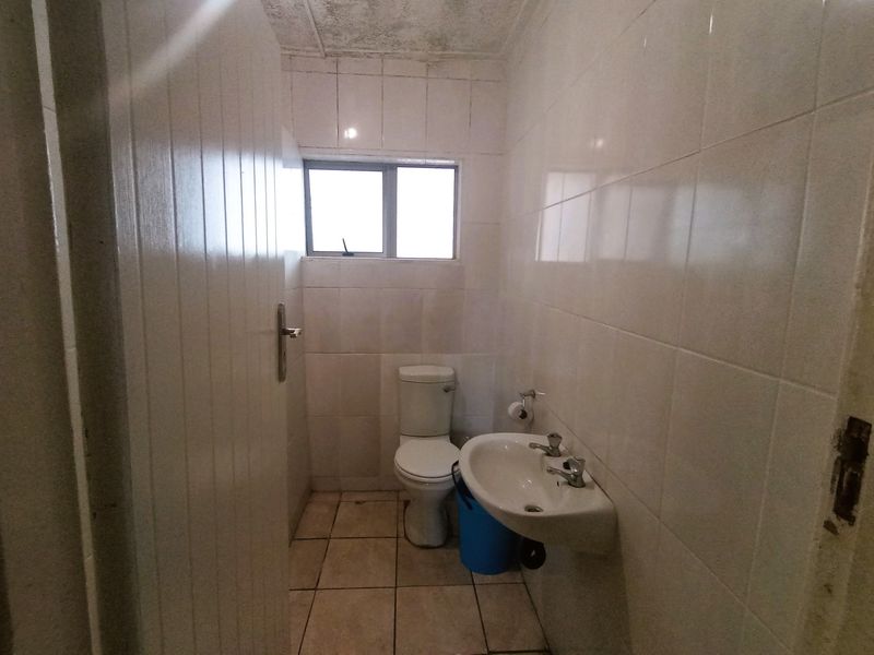 A compact bathroom featuring tiled walls and flooring, a pedestal basin, and a standard toilet, requiring cosmetic updates and maintenance.
