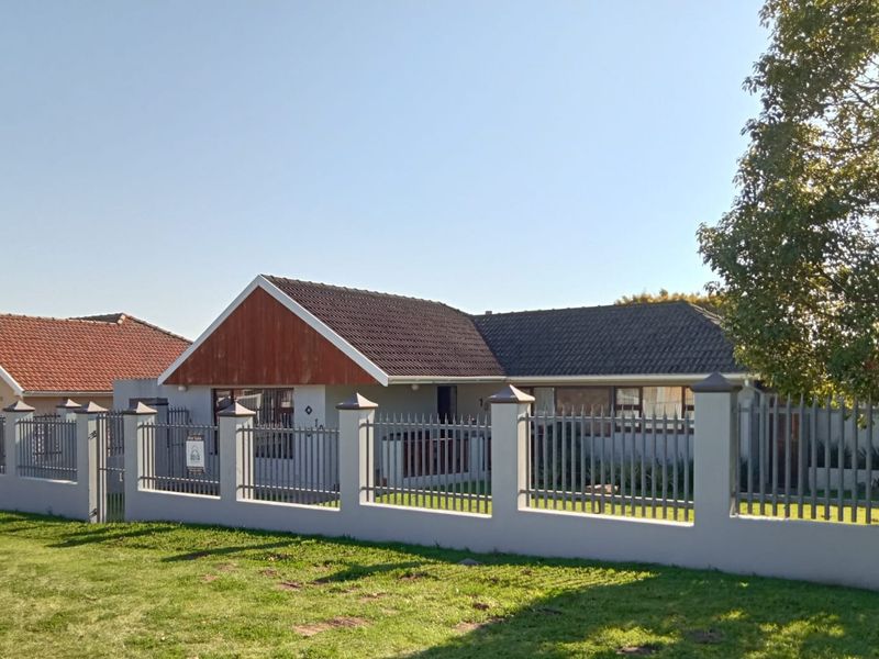 Front elevation of a single-story house featuring a tiled roof, timber gable detail, and a secure perimeter wall with metal fencing.