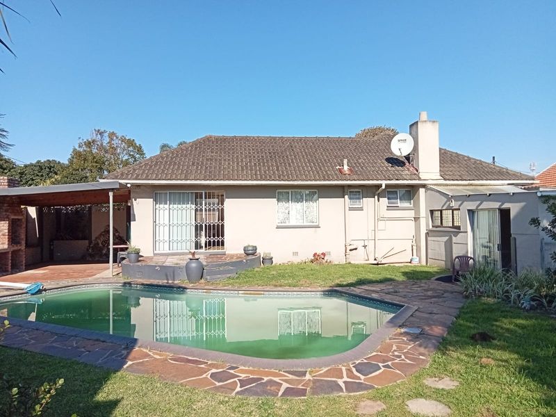 Rear view of the property featuring a swimming pool, covered patio area with built-in braai, and a tiled roof structure.
