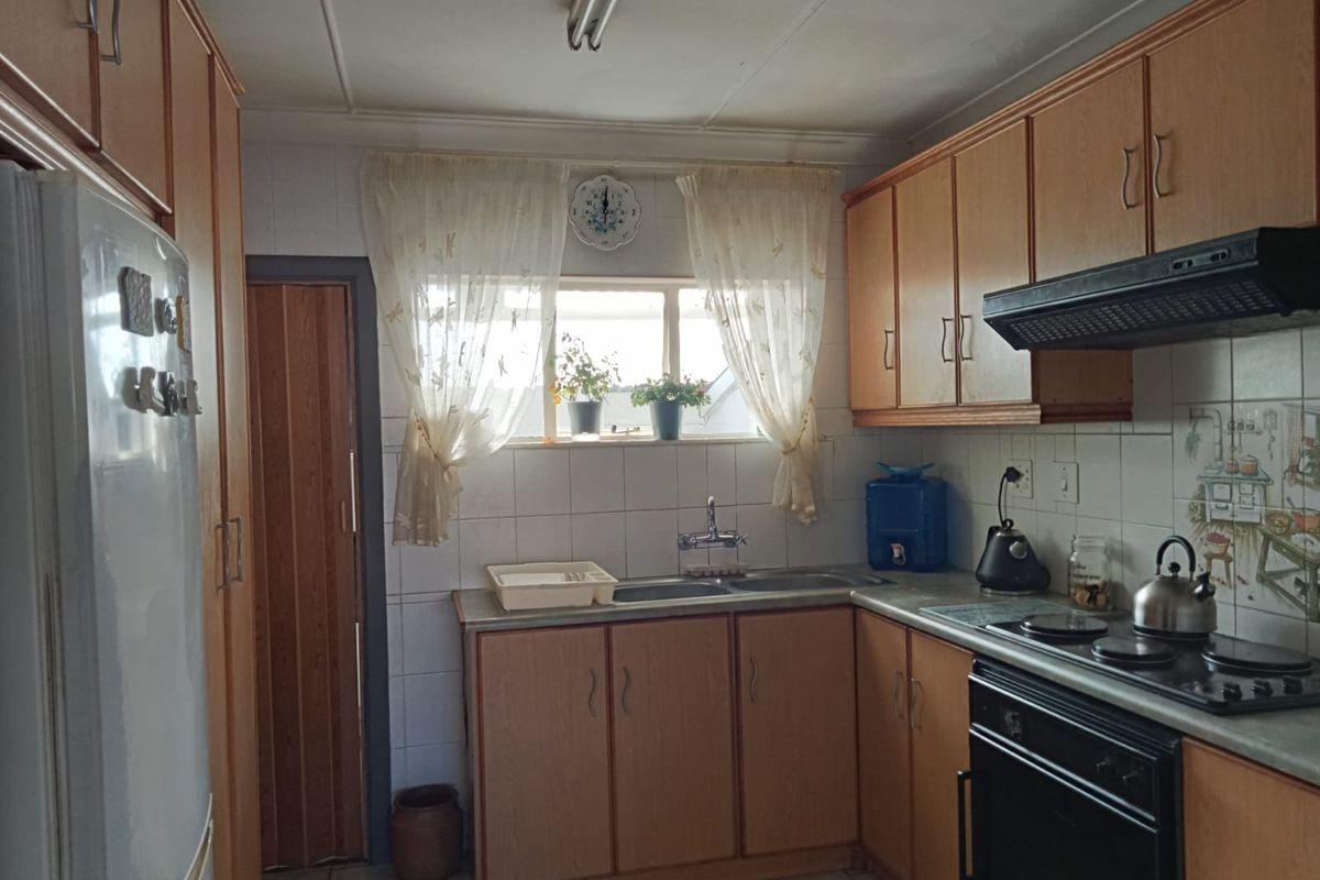 A functional kitchen featuring laminate cabinetry, built-in oven with hob, extractor fan, and tiled backsplash, offering a practical layout with potential for modern updates.