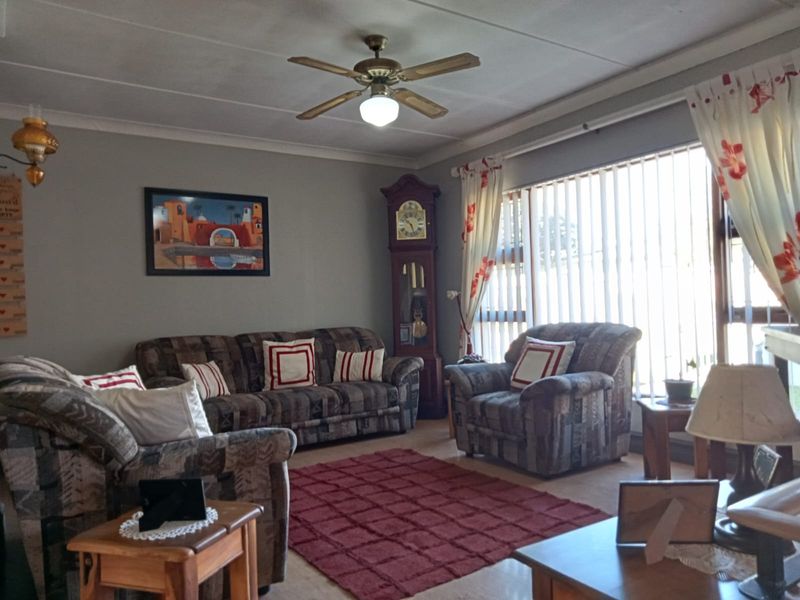 A comfortable living room featuring a ceiling fan, coved ceilings, and large windows with vertical blinds, providing ample natural light.