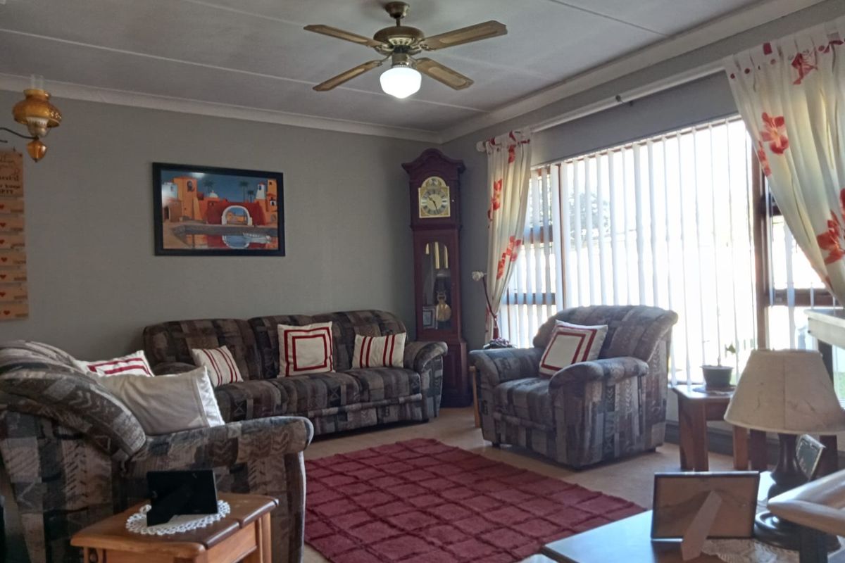 A comfortable living room featuring a ceiling fan, coved ceilings, and large windows with vertical blinds, providing ample natural light.