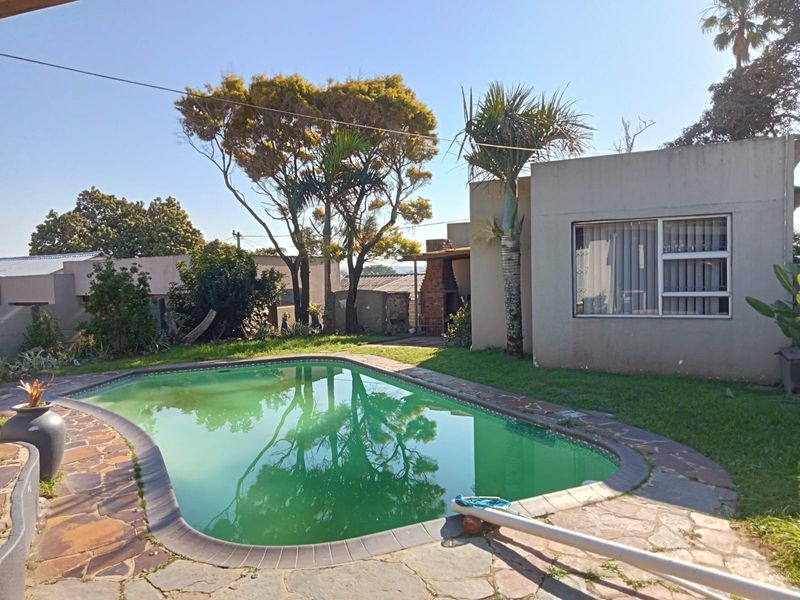 Outdoor pool area featuring stone paving, a built-in braai, and established garden surroundings, providing a functional space for outdoor entertainment.