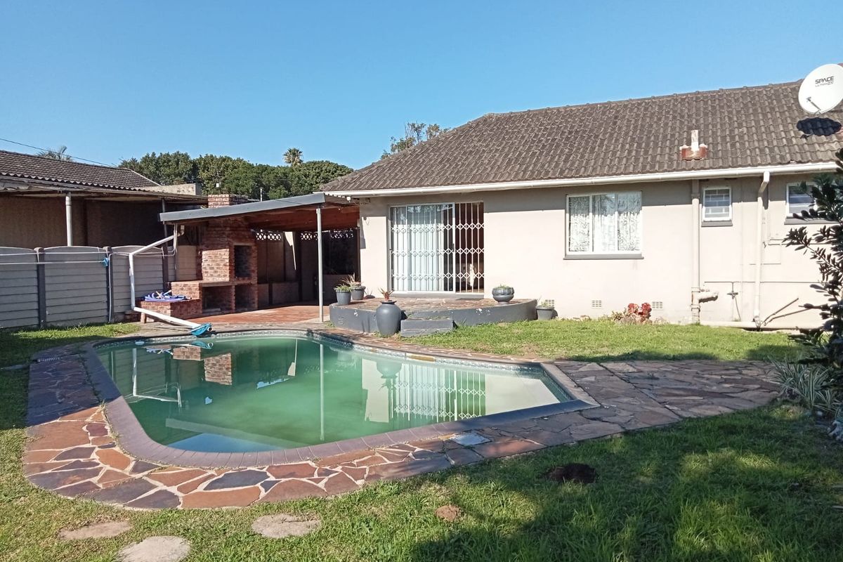 Rear exterior view featuring a swimming pool, stone-paved surround, and a covered patio area with a built-in brick braai.